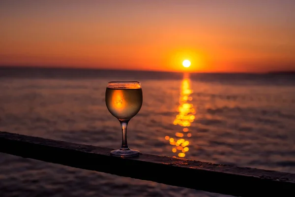 在大海的夕阳西下 一杯白葡萄酒在水面上闪烁着美丽的光芒 — 图库照片