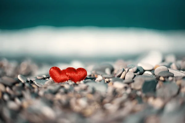 海岸のぼやけた背景の石の上に赤いハートが2つ 愛のシンボル — ストック写真