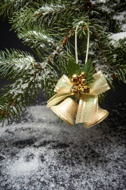 Çanları olan bir Noel süslemesi, Noel ağacının bir dalı ve siyah arka planda yapay kar.
