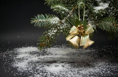 Çanları olan bir Noel süslemesi, Noel ağacının bir dalı ve siyah arka planda yapay kar.