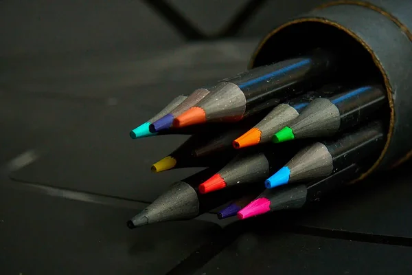 Set di matite colorate in un astuccio di cartone rotondo su sfondo scuro. — Foto Stock