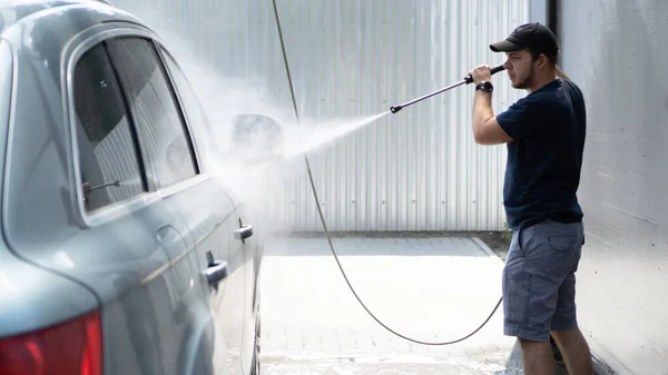 Mannen tvättar bilen med högtryckstvätt. Vattenstråle under tvättprocessen på självbetjäning biltvätt — Stockfoto