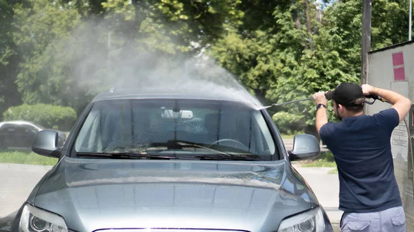 Mannen tvättar bilen med högtryckstvätt. Vattenstråle under tvättprocessen på självbetjäning biltvätt — Stockfoto