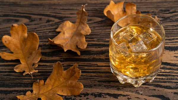 Alcoolisme, alcool dans un verre et feuilles d'automne sur une table en bois. L'alcoolisme. Alcool brun dans le verre — Photo