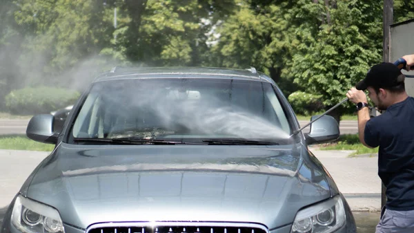 Mannen tvättar bilen med högtryckstvätt. Vattenstråle under tvättprocessen på självbetjäning biltvätt — Stockfoto
