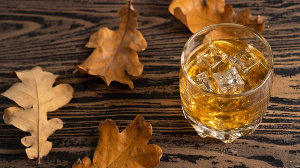 Imagem conceitual sobre o alcoolismo. Uísque em um copo e folhas de outono em uma mesa de madeira — Fotografia de Stock
