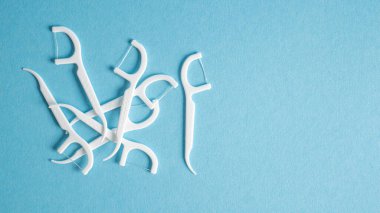 Mavi arka planda diş ipi izleri var. Yumuşak diş ipi kazmaları. Diş kıracağı. Diş ipli plastik beyaz bir kürdan.
