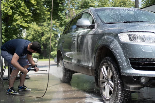 Mannen som tvättar bildäck. Biltvätt med högtryckstvätt. Självbetjäning biltvätt. Rengöringsbil med högtrycksvatten — Stockfoto