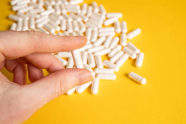 Sarı arka planda beyaz kapsülü tutan el. Yiyecek takviyesi. D3 vitamini. Magnezyum destek kapsülleri