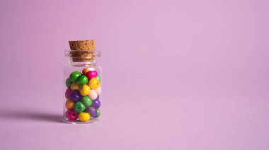 Çok renkli boncuk topları olan cam bir kavanoz. Küçük cam şişedeki ahşap toplar Pembe arka planda tıpası olan