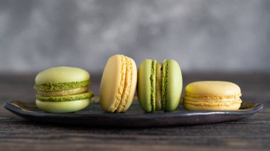 Gri arkaplanda yazı alanı olan güzel bir yaprak tabaktaki canlı yeşil ve sarı badem kurabiyeleri.