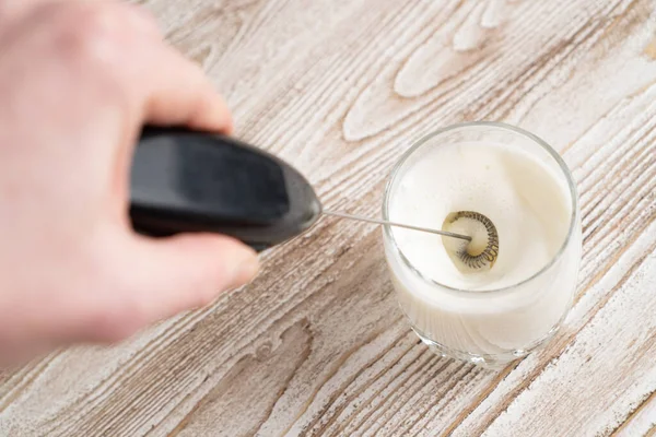 Using milk frother device in glass, closeup. Milk handheld mixer. Glass of milk on wooden table — Stock Photo, Image