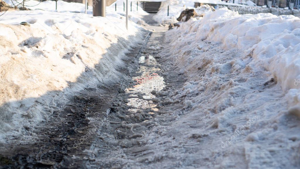 Dirty melting snow in the city streets. Spring creek flows through the asphalt. Large snowdrifts. Pedestrians obstacles 