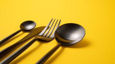 Sarı arka planda tamamen siyah çatal bıçak takımı. Şık metal yemek kaşığı, çay kaşığı, çatal ve bıçak.. 