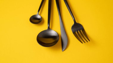 Siyah mutfak çatal bıçak takımı. Sarı bez üzerinde şık sofra takımı. Siyah çatal bıçaklı sarı arkaplan