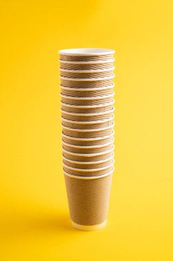 Kağıt bardak yığını. Sarı arka planda kahverengi kağıt bardaklar. Tek kullanımlık kağıt bardak. Atık geri dönüşüm kavramı