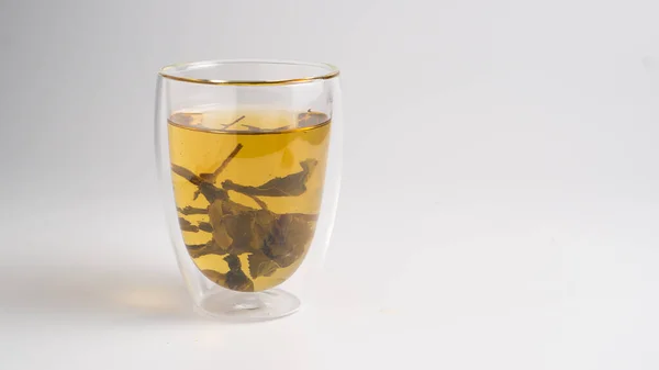 Oolong beyaz arka planda çay fincanına çay bırakır. Bardakta yeşil çay. Seylan çayı yapraklı şeffaf bir fincan.