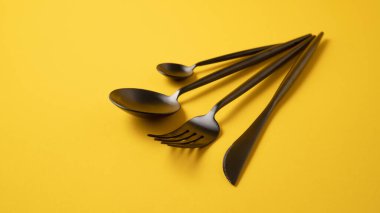 Siyah mutfak çatal bıçak takımı. Sarı bez üzerinde şık sofra takımı. Siyah çatal bıçaklı sarı arkaplan