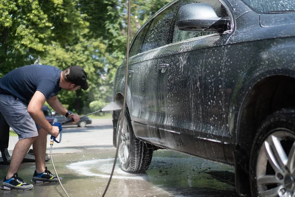 Mannen som tvättar bildäck. Biltvätt med högtryckstvätt. Självbetjäning biltvätt. Rengöringsbil med högtrycksvatten — Stockfoto