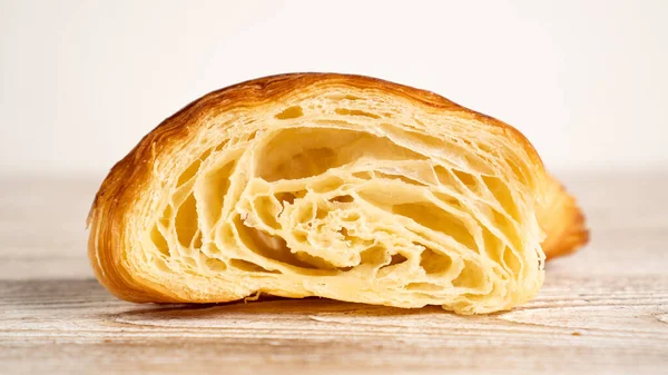 Frisch gebackenes Croissant halbiert auf hellem Holztisch. Croissant in der Bildmitte — Stockfoto