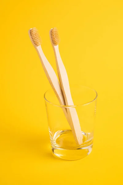 Wooden toothbrushes in a transparent glass on a yellow background. Bamboo toothbrushes as an eco concept. Vertical image — Stock Photo, Image