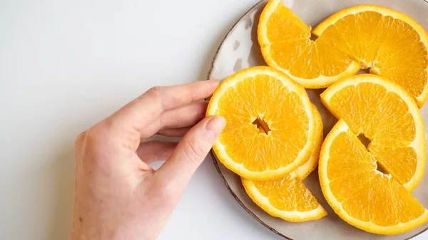 Mão pegando uma fatia de laranja do prato na mesa. Fatia de laranja na mão. Laranja suculenta em uma chapa cinza — Fotografia de Stock