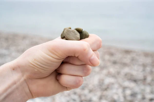 Hand holding grey stones in the ice cream cone. Vacation mood. Natural toys on the seashore.