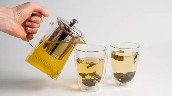 Oolong leaves tea in a teacup on white background. Pouring green tea from a glass teapot in double-walled glasses. High quality photo
