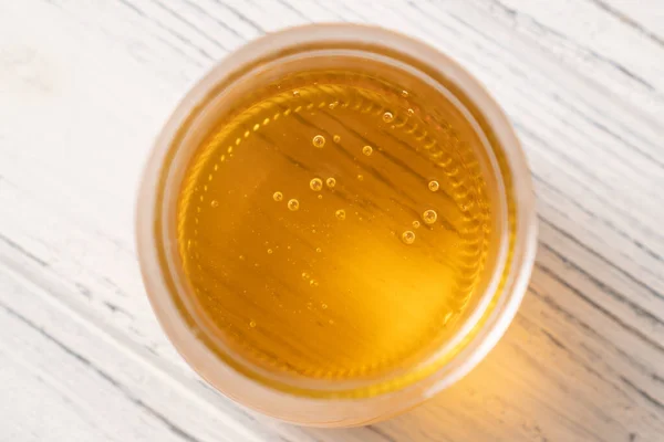 Bolhas de mel num frasco de vidro. Vista superior sobre mel natural em um frasco de vidro aberto. Mel amarelo na mesa de madeira branca — Fotografia de Stock