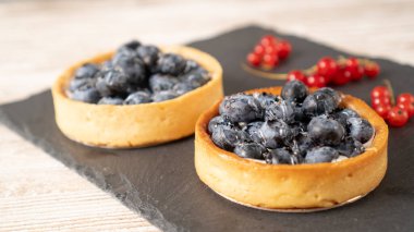 Siyah tabakta iki yabanmersinli tart. Küçük limonlu yaban mersinli tart. Pastayı böğürtlenle kapat.