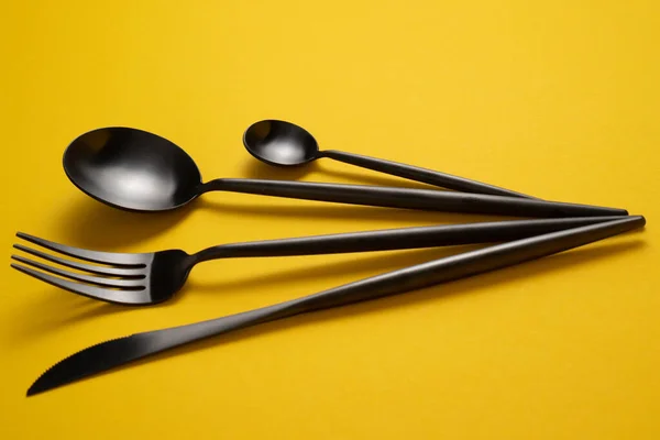 Black tableware on yellow tablecloth. Black flatware on yellow tablecloth. Black cutlery on yellow tablecloth — Stock Photo, Image