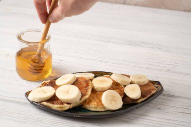 Beyaz ahşap bir masada Ricotta krepleri. Muzlu krep. El bal kaşığıyla
