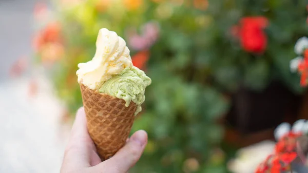 Mão segurando sorvete de cor dupla em cone na rua. O melhor cone de gelado. Gelato de pistache. Gelado de manga — Fotografia de Stock