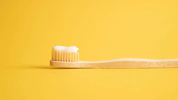 Eco dental concept. Natural toothpaste on a bamboo toothbrush. Wooden toothbrush on yellow background with copy space — Stock Photo, Image