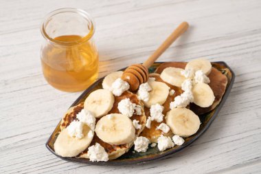 Beyaz ahşap bir masada Ricotta krepleri. Süzme peynirli ve muzlu krep. Kahvaltıda bal kavanozu