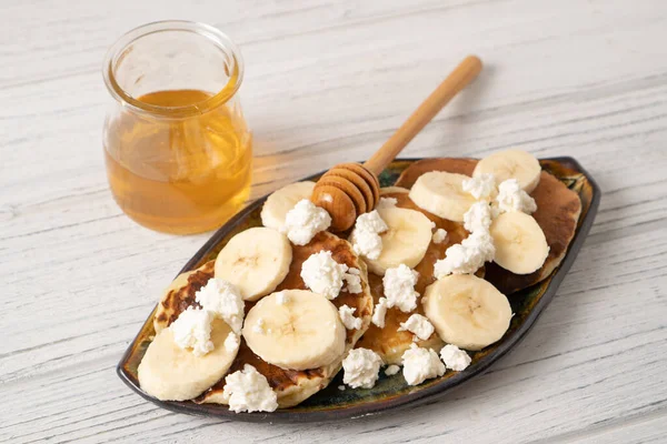 Beyaz ahşap bir masada Ricotta krepleri. Süzme peynirli ve muzlu krep. Kahvaltıda bal kavanozu