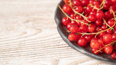 Siyah kasede kuşüzümü. Ahşap masada siyah tabakta kırmızı frenk üzümü. Kırmızı ve siyah. Kırmızı küçük meyveler
