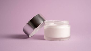 Beyaz nemlendirici fotoğraf. Nemlendiriciyi mor arka planda cam kapta kapat. Şeffaf kavanozda krema