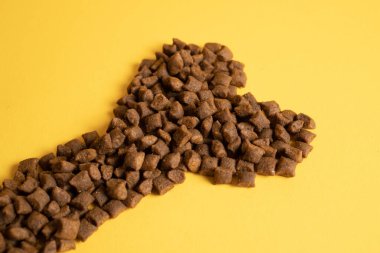 Kemik şeklinde kedi maması yığını. Sarı arka planda kemik şeklinde kedi maması. Kemik şeklinde evcil hayvan yiyeceği.