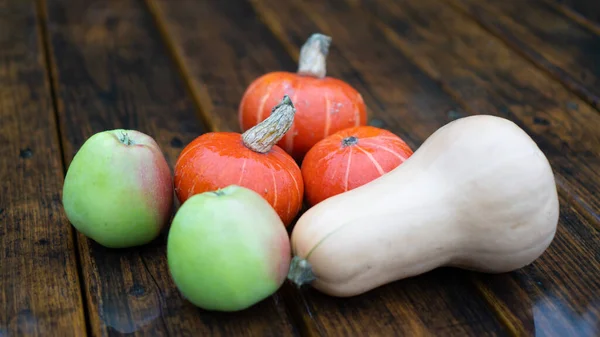Осенние фрукты и овощи. Ореховая тыква и тыква на деревянном столе. Падение яблок с каплями дождя — стоковое фото