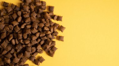Sarı arka planda izole edilmiş kedi maması yığını. Sağ taraf kopyalama alanı. Hayvan mamasının en üst görüntüsü