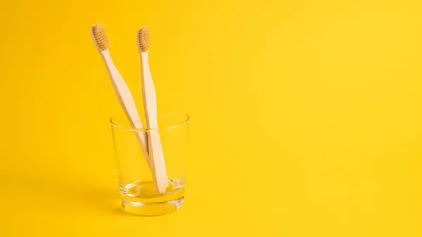 Wooden toothbrushes in a transparent glass on a yellow background. Bamboo toothbrushes as an eco concept — Stock Photo, Image