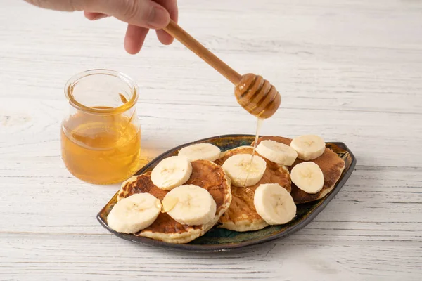 Käsepuffer mit Banane und Honig. Ricotta-Pfannkuchen mit Joghurt und Banane. Hand hält Honiglöffel — Stockfoto