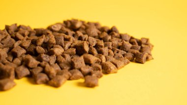 Kedi maması yığını. Kedi maması sarı arka planda izole edilmiş. Kare kuru kedi maması. Altın arka planda kahverengi evcil hayvan yiyeceği
