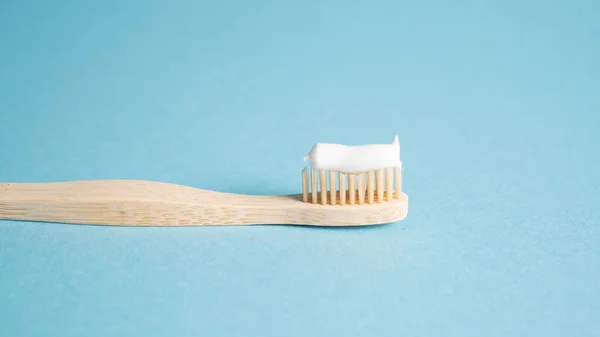 Eco dental concept. Natural toothpaste on a bamboo toothbrush. Wooden toothbrush on blue background with copy space — Stock Photo, Image