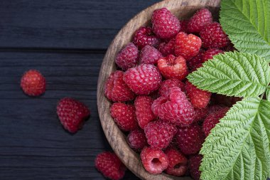 Koyu ahşap arka planda taze, kırmızı ahududular. Yeşil yapraklar. Metin için yer