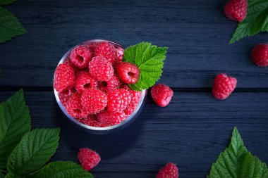 Koyu ahşap arka planda taze, kırmızı ahududular. Yeşil yapraklar. Metin için yer