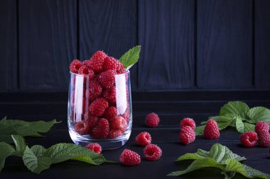 Koyu ahşap arka planda taze, kırmızı ahududular. Yeşil yapraklar. Metin için yer