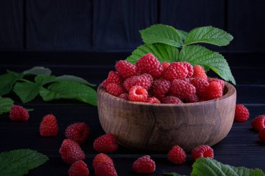 Koyu ahşap arka planda taze, kırmızı ahududular. Yeşil yapraklar. Metin için yer