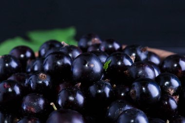 Siyah frenk üzümü ve koyu ahşap arka planda yeşil yapraklar. Frenk üzümü ve yeşil yapraklı arka plan. Frenk üzümü makrosu.